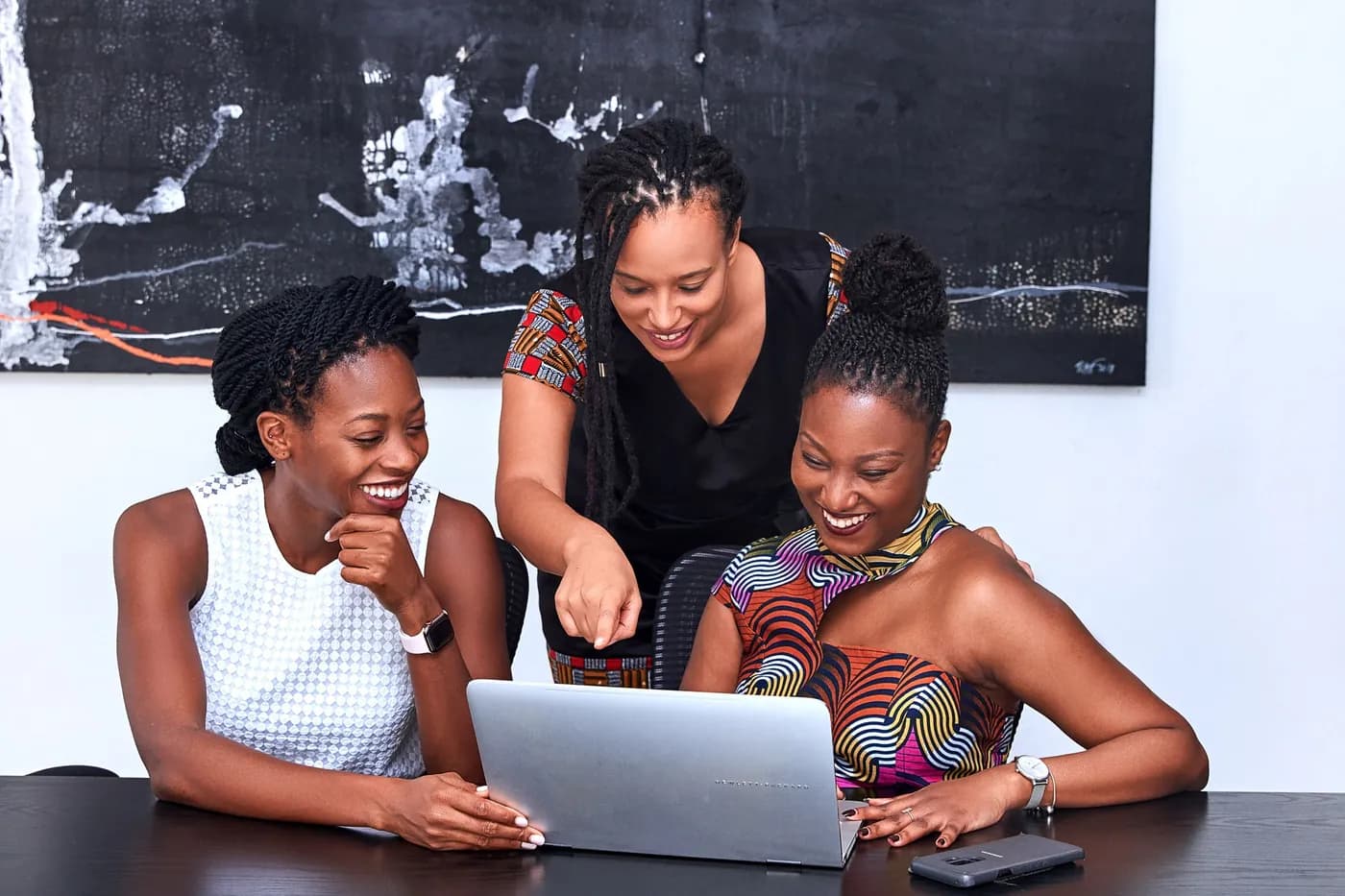 Three women working together over a laptop, one pointing at the screen.